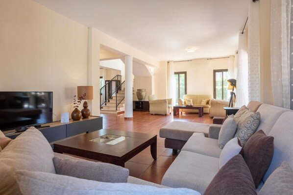 A spacious living room with a flat-screen TV, comfortable seating, and a staircase leading to another level. - Villa Iliana - Four Bedroom Villa, Sleeps 8 (Poli Crysochous)