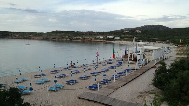 A beach with rows of blue sun loungers and a wooden walkway leading to a building labeled "Welcome". - Scirocco House | Sea View Terrace (Isola Rossa)