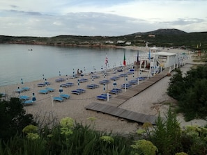 A beach with rows of blue sun loungers and a wooden walkway leading to a building labeled "Welcome". - Scirocco House | Terrace with a view of the sea (Isola Rossa)