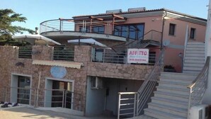 A two-story building with a stone facade, a balcony, and a staircase leading to the upper floor. - Scirocco House | Sea View Terrace (Isola Rossa)