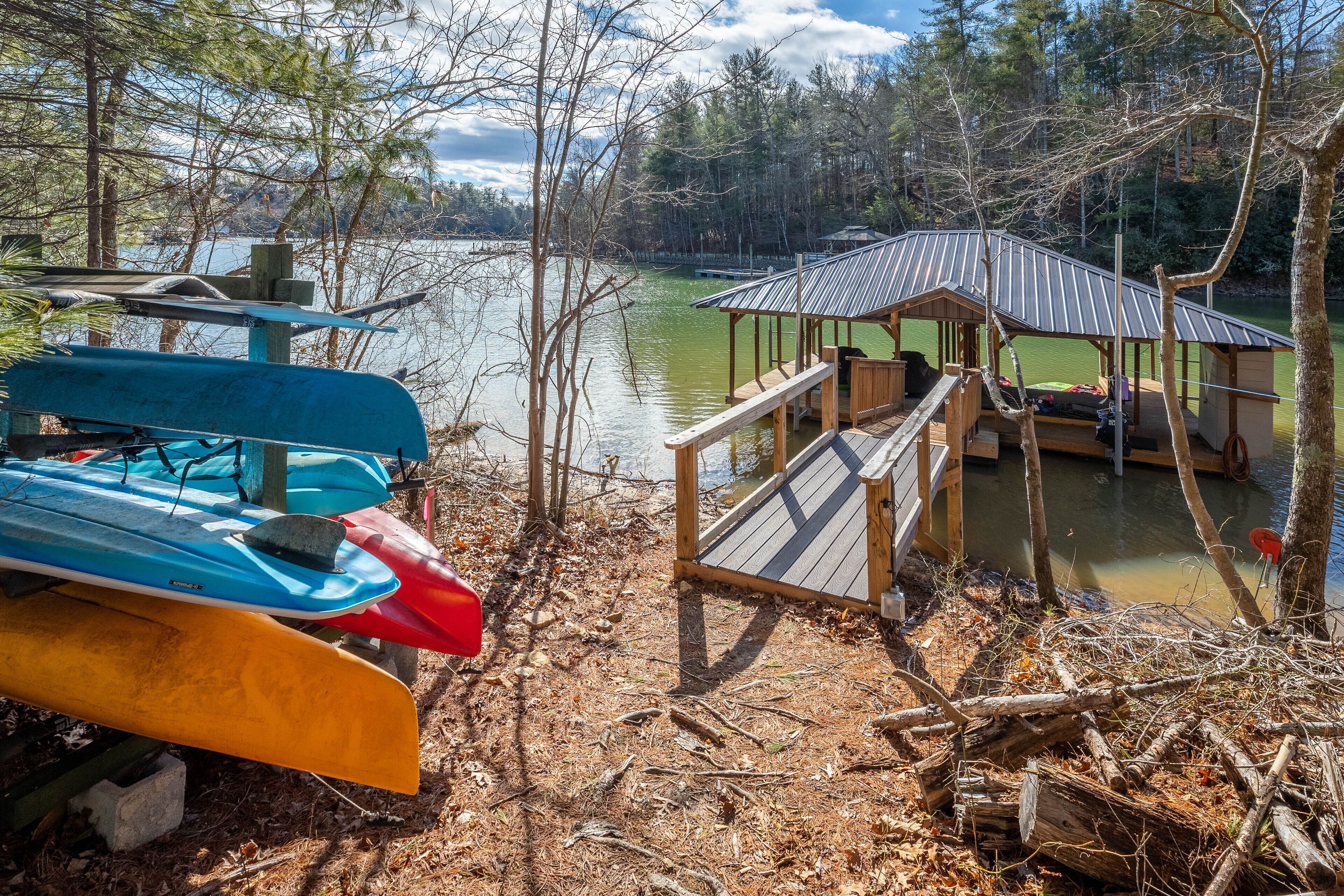 A dock with canoes and a covered pavilion by a lake surrounded by trees.