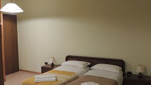 A hotel room with two single beds, a wooden nightstand with a lamp, a wooden table, and a door. - La Via Antiga - Apartment # 2 (Torre di Mosto)