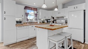 A modern kitchen with white cabinets, a wooden countertop, and a central island with stools. - Located near Mt. Rushmore, the Black Hills, Badlands National Park & more!! (Hermosa)
