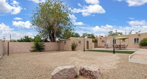 A residential property with a gravel yard, a patio with outdoor furniture, and a large tree. - The Dartmouth House S (Albuquerque)