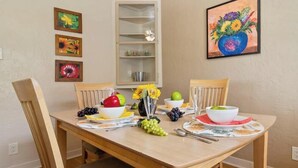 Uma mesa de jantar com cadeiras, um vaso com flores e diversas frutas e legumes.