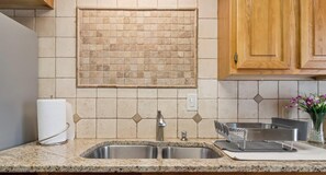 A kitchen with a granite countertop, stainless steel sink, and wooden cabinets. - The Dartmouth House S (Albuquerque)