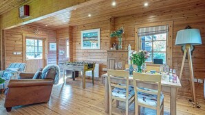 Un accogliente interno di una baita con pareti in legno, un tavolo da calcio, un'area pranzo con sedie e un tavolo imbandito per due e un divano nella zona giorno.