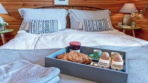 Una camera da letto accogliente con una parete in legno, un letto con cuscini decorati, un comodino con una lampada e un vassoio con cibo e bevande.