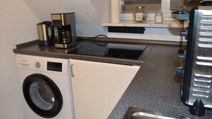 A compact kitchen with a washing machine, a coffee maker, and a stove.