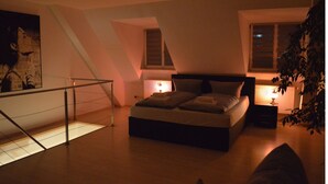 A bedroom with a bed, bedside lamps, a radiator, a window, and a plant.