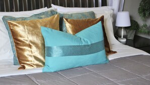 Een bed met een grijze quilt, een zwart hoofdeinde en decoratieve kussens in goud en teal.