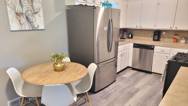 Een moderne keuken met witte kastjes, een roestvrijstalen koelkast, een vaatwasser en een ronde houten tafel met twee witte stoelen.