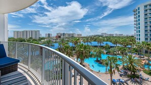 A balcony with a view of a pool area, including palm trees and a blue-roofed building. - NEW Updated Condo~HUGE Lagoon Pool~Balcony~SplashPad~Full2BR Palms Resort #1515 (Destin)