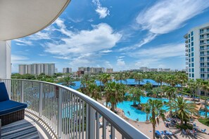 Uma varanda com vista para área da piscina, incluindo palmeiras e um edifício com telhado azul.