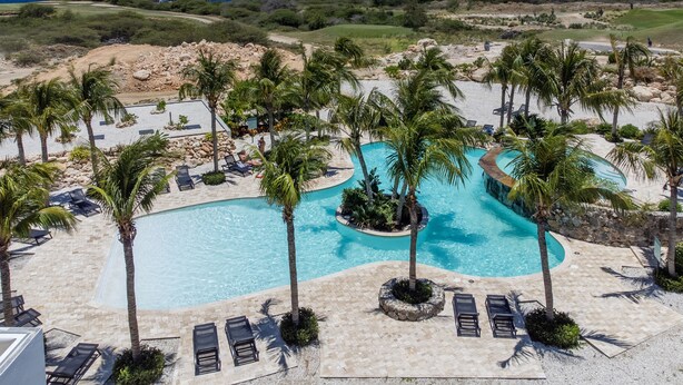 Un resort con una grande piscina circondata da palme, lettini e vista sull'oceano.