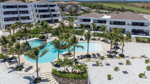 Un resort con diversi edifici bianchi, una piscina centrale e palme.
