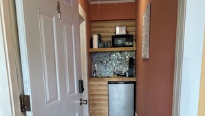 Um corredor estreito com uma área de cozinha, incluindo uma geladeira, micro-ondas e prateleiras de madeira.