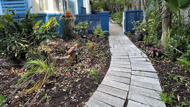Uma trilha que leva a uma casa azul com jardim e árvores.