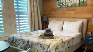 Quarto com cama, cadeira, mesa, mesa de cabeceira e um quadro na parede.