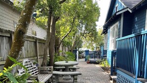 Uma trilha pavimentada leva a um banco de madeira e uma mesa para piquenique, tudo cercado por vegetação exuberante e uma cerca azul.