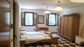 A bedroom with two beds, a wooden wardrobe, a desk, and a window with a view of greenery. - La Via Antiga - Apartment # 1 (Torre di Mosto)