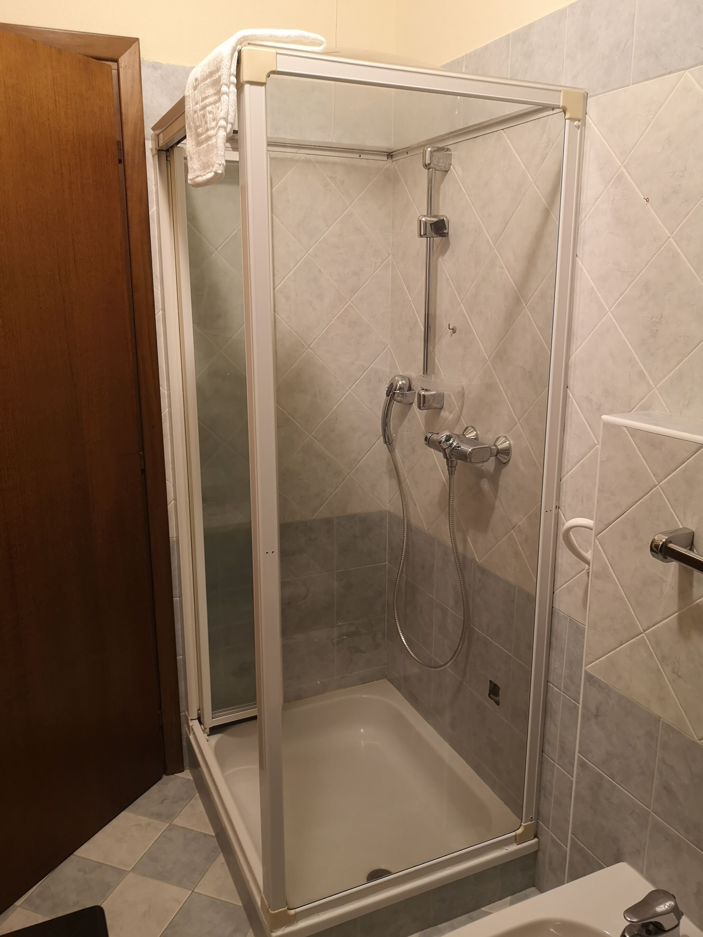 Eine gläserne Duschkabine mit einer weißen Badewanne, ein Handtuch an der Tür und geflieste Wände.