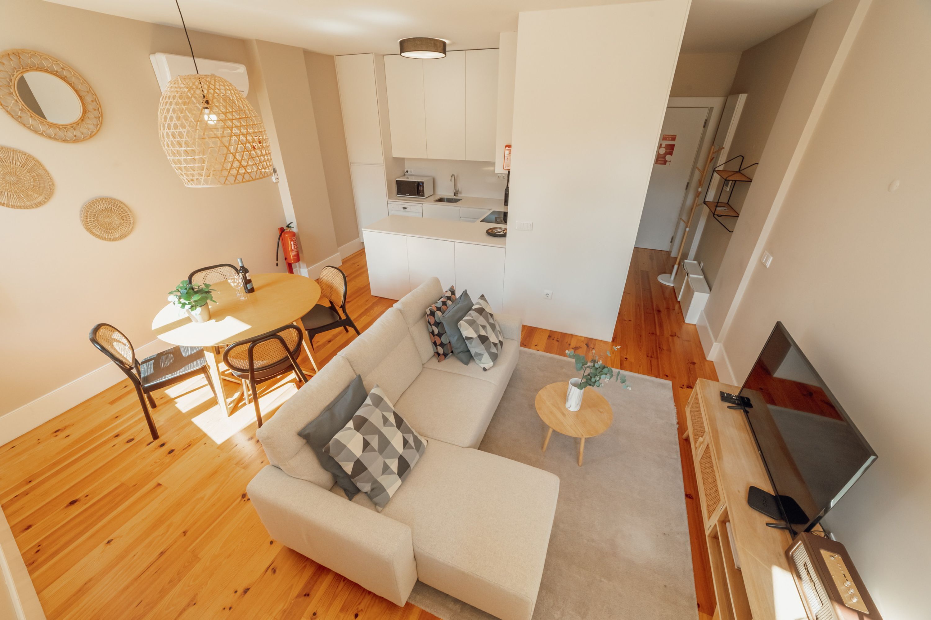 Een moderne woonkamer met een bank, salontafel en tv-meubel. Er is een eethoek met een tafel en stoelen. De keuken is op de achtergrond te zien, met witte kasten en een magnetron.