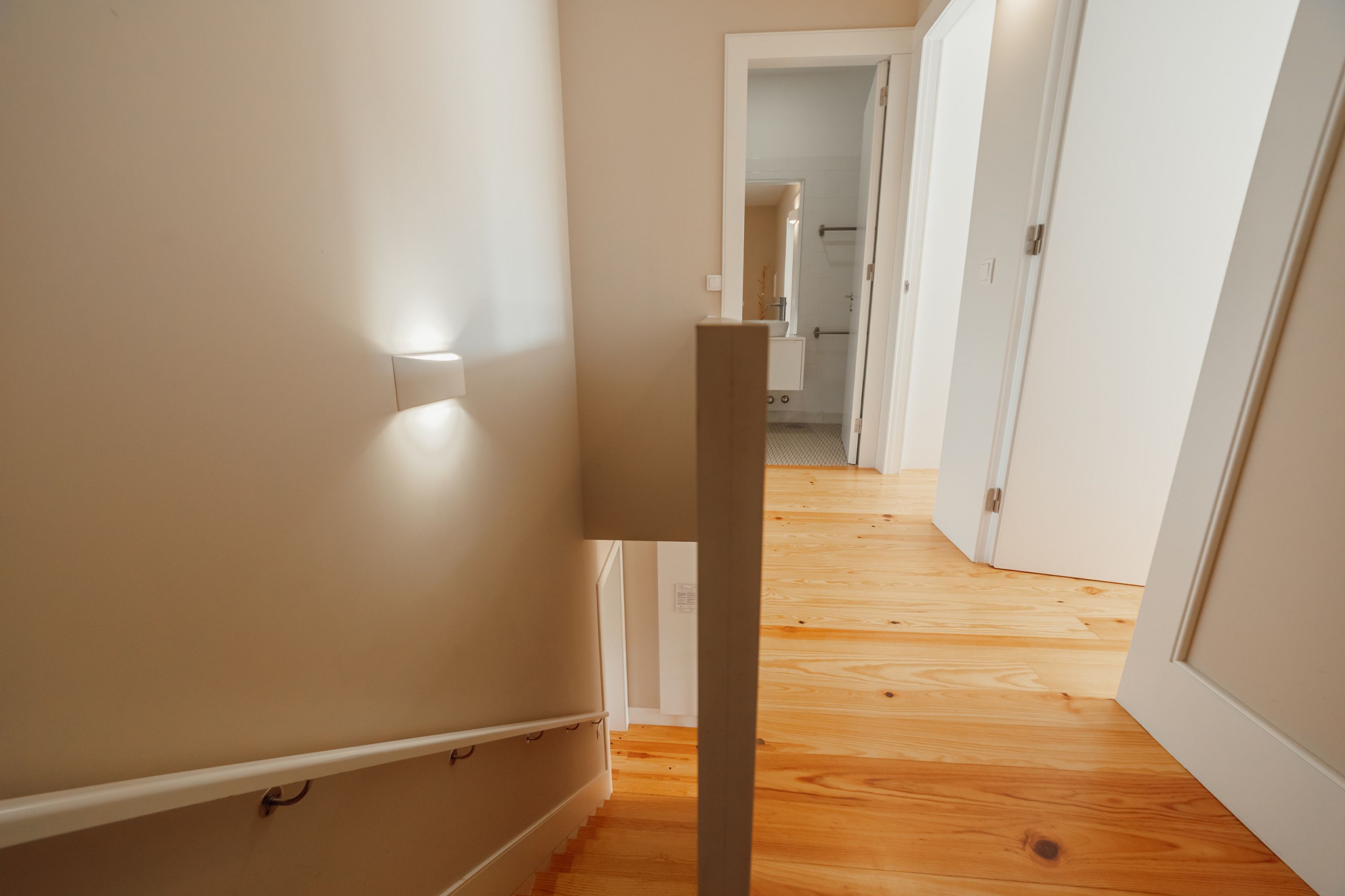 A hallway with wooden flooring and white walls, leading to a bathroom with a shower and a toilet.