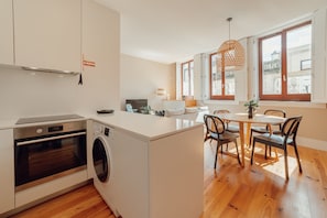 A modern kitchen with a built-in oven, washing machine, and dining area with a table and chairs. - Boavista Premium II Duplex Terrace by Vacationy (Porto)