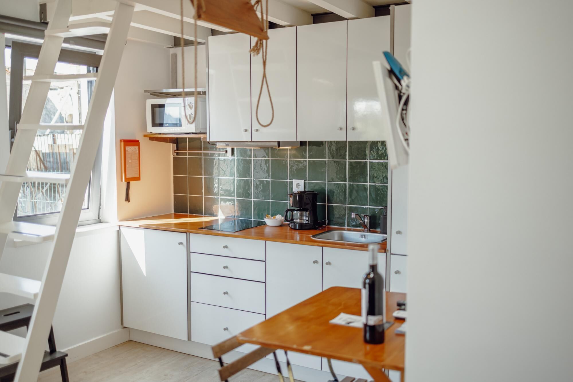 Een keuken met witte kastjes, een houten aanrecht, een magnetron, een koffiezetapparaat en een fles wijn op een tafel.