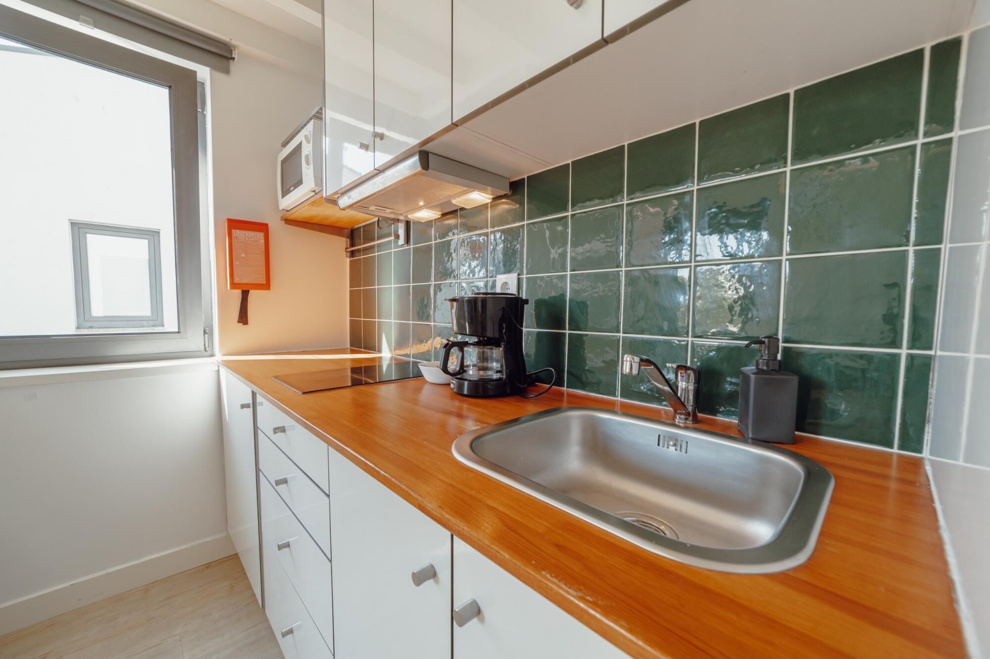 Une cuisine moderne dotée d’un plan de travail en bois, d’un évier en acier inoxydable et d’un dosseret de carrelage vert.