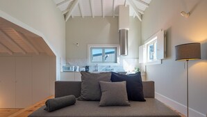 A modern living room with a grey sofa, a window with a view, a kitchen in the background, and a floor lamp. - Oporto Rooftop Studio by Vacationy (Porto)