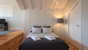 A bedroom with a bed, bedside lamps, a wooden dresser, and a TV on a stand. - Oporto Rooftop Studio by Vacationy (Porto)