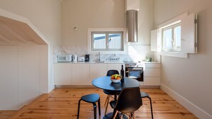 A modern kitchen with white cabinets, a black dining table, and a window overlooking the city. - Oporto Rooftop Studio by Vacationy (Porto)