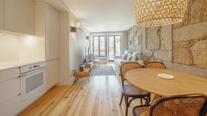 Eine moderne Küche mit weißen Schränken, einem Holztisch, Korbstühlen und einer Steinwand.