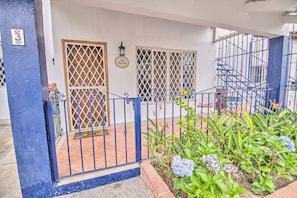 Un patio amurallado con cerca de metal azul, suelo de baldosas y diversas plantas, entre ellas hortensias.