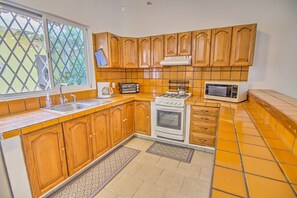 A kitchen with wooden cabinets, a gas stove, a microwave, and a window with a view of greenery. - Groundfloor 2BR with Private Pool: Palmas 3B (Bucerías)