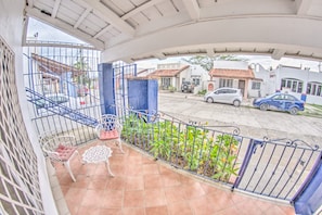 En balkon med udsigt over en boligkvarter, en hvid stol og et lille bord med hvide blonde.'