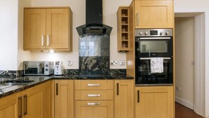 A kitchen with wooden cabinets, a black range hood, a built-in oven, and a microwave. - Homely 3 Bedroom in the Heart of Central Edinburgh (Edinburgh)