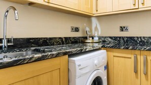 A kitchen with wooden cabinets, a granite countertop, a sink, and a front-loading washing machine. - Homely 3 Bedroom in the Heart of Central Edinburgh (Edinburgh)