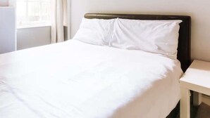 A neatly made bed with white bedding in a room with a window and a bedside table. - Homely 3 Bedroom in the Heart of Central Edinburgh (Edinburgh)