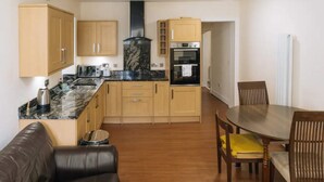 A compact kitchen with wooden cabinets, a black marble countertop, and a built-in oven. - Homely 3 Bedroom in the Heart of Central Edinburgh (Edinburgh)