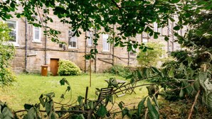A courtyard with a stone building, a wooden bench, and overgrown vegetation. - Stylish 3 Bedroom Apartment Near Hollyrood Park (Edinburgh)