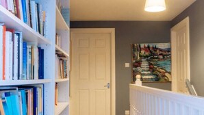 A hallway with wooden flooring, white bookshelves, and a white railing. - Stylish 3 Bedroom Apartment Near Hollyrood Park (Edinburgh)