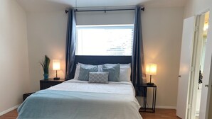 Une chambre à coucher bien rangée, avec un lit, deux tables de chevet, une fenêtre avec des rideaux et une porte.