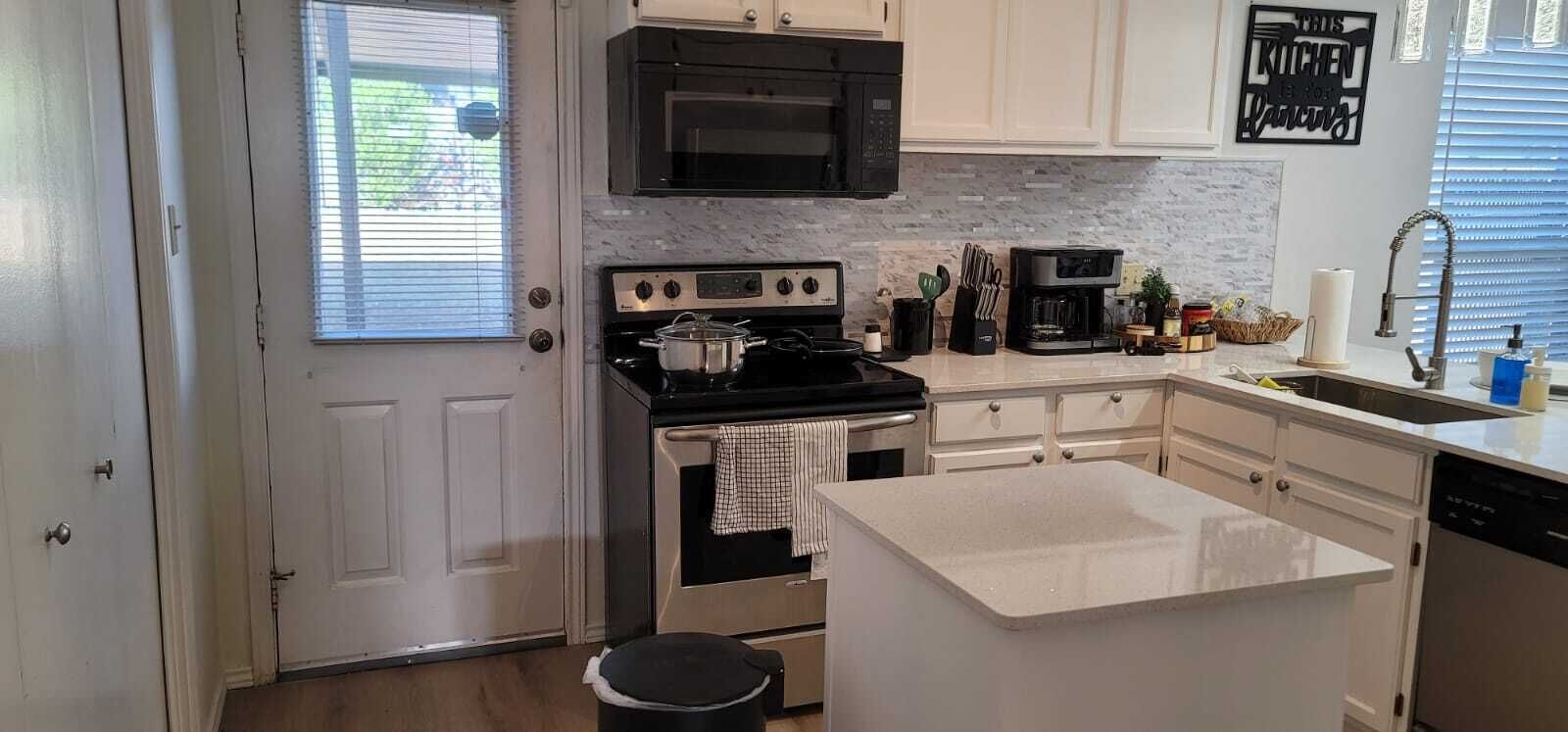 A compact kitchen with white cabinets, a black stove, a microwave, and a coffee maker.