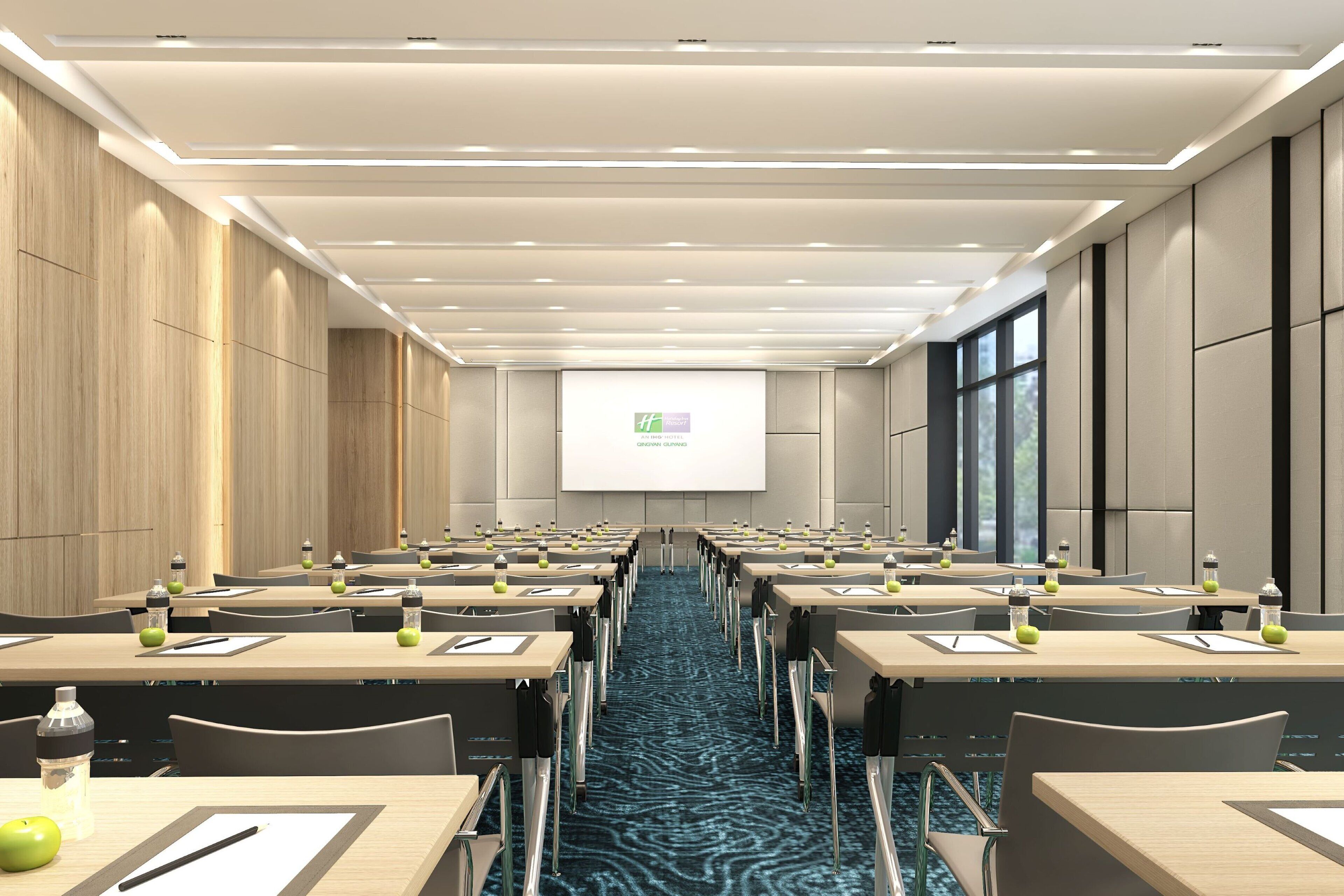 Une salle de conférence avec des rangées de tables, des chaises et un écran de projection à l’avant.