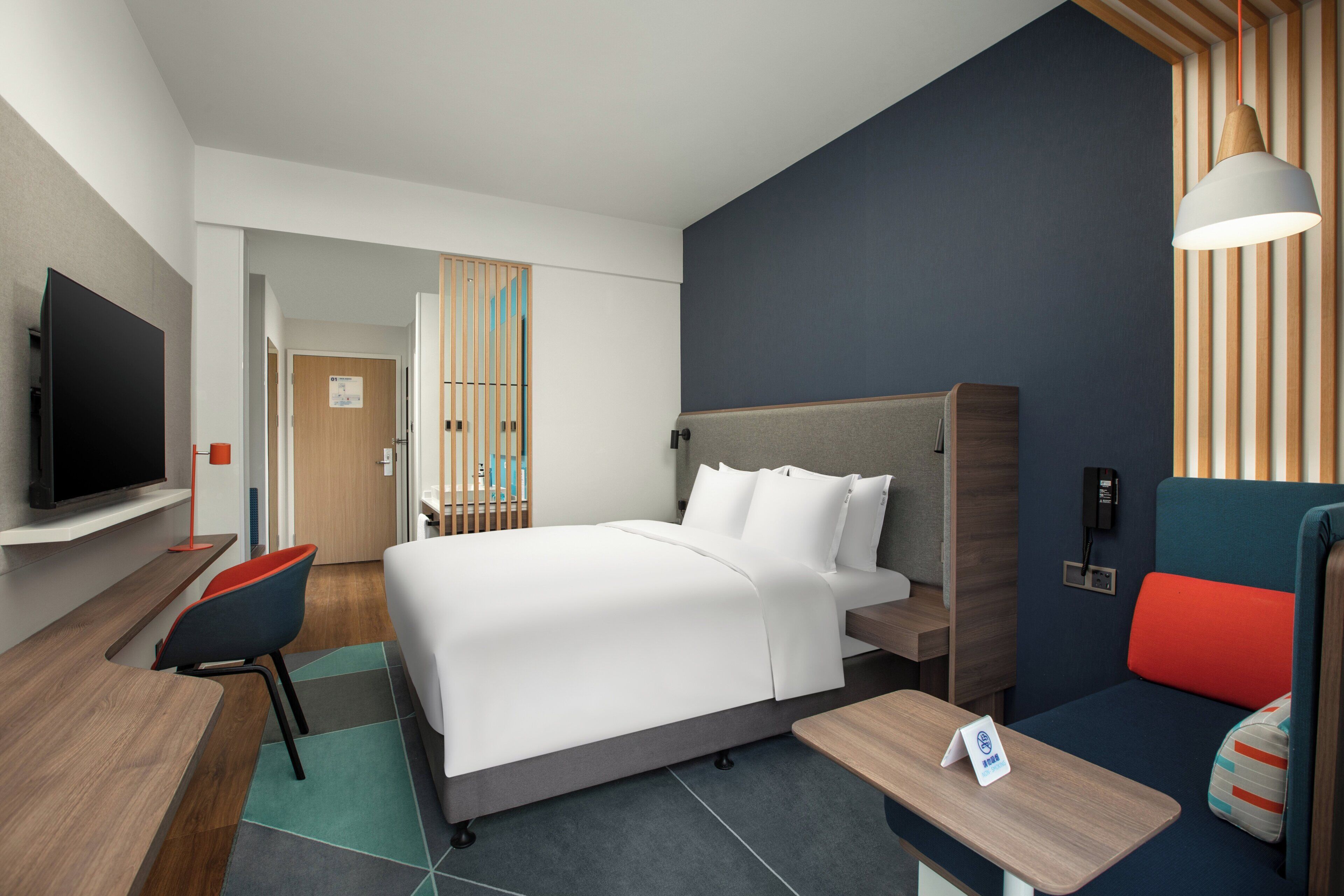 Quarto de hotel moderno com cama, escrivaninha, televisão e área de estar.