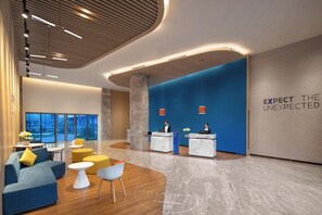 A modern reception area with a blue accent wall, a marble reception desk, and a seating area with sofas and ottomans. - Holiday Inn Express Guiyang Qingyan by IHG (Guiyang)