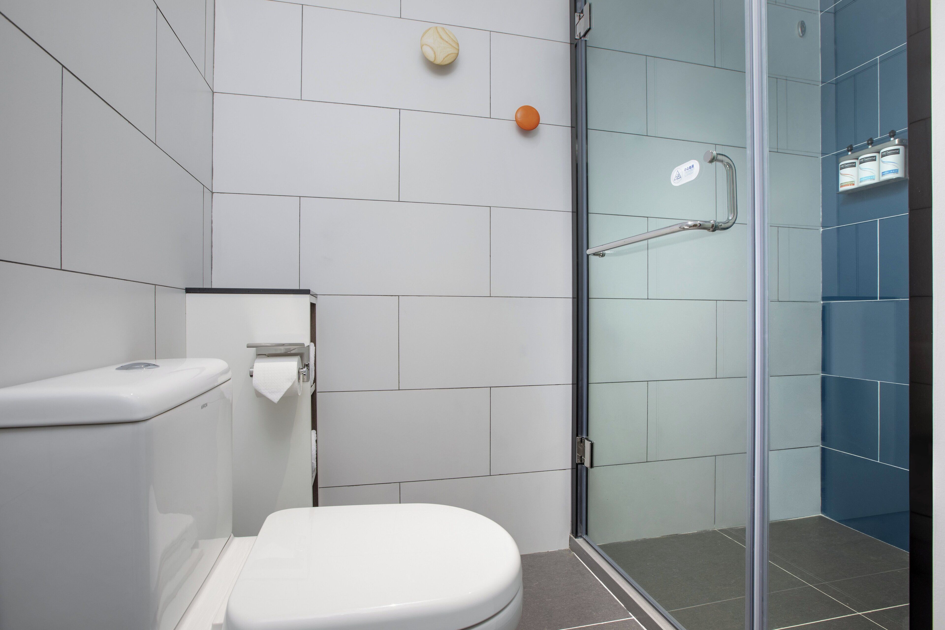 Een moderne badkamer met toilet, een glazen douchecabine en een handdroger.
